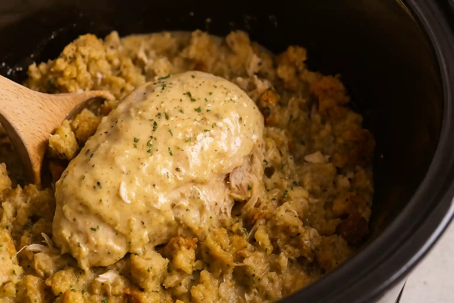 Tender shredded chicken with golden stuffing in a rustic crockpot, garnished with herbs and steam rising.