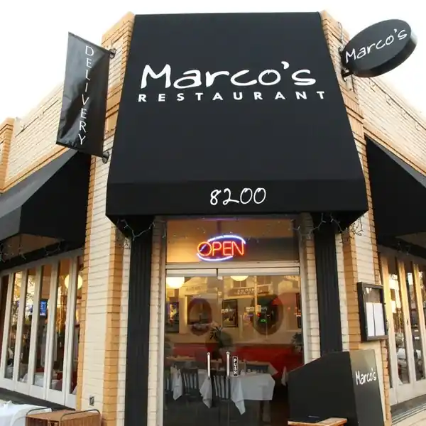 Front exterior of Marco’s Restaurant with black awning, bold white signage, neon “OPEN” sign above the entrance, and large windows revealing indoor dining setup.