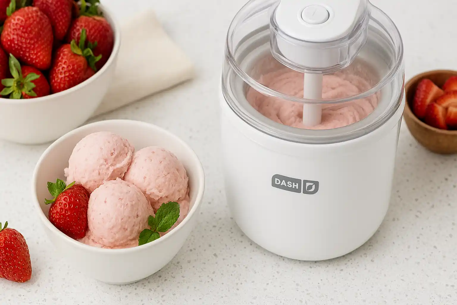 Fresh strawberry ice cream made in a Dash ice cream maker on a modern kitchen counter with ripe strawberries and mint garnish.
