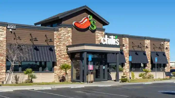 Exterior of a Chili’s restaurant with stone and wood siding, black awnings, the red chili pepper logo, and visible street number 11910, with handicap parking signs in front.