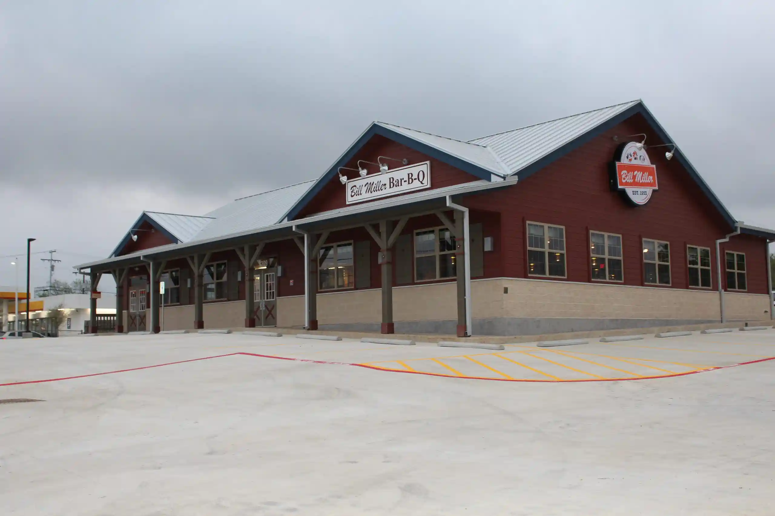 Exterior of a Bill Miller Bar-B-Q restaurant featuring a red and beige building with a covered walkway supported by wooden beams.