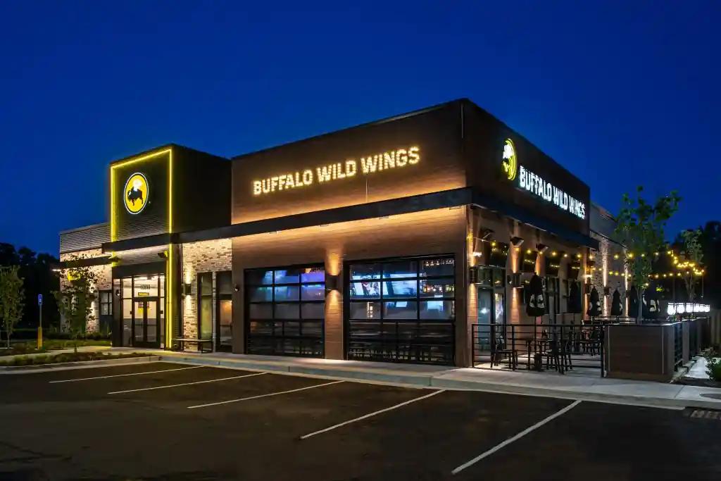 Exterior view of a Buffalo Wild Wings restaurant at night with illuminated signage and outdoor seating area.