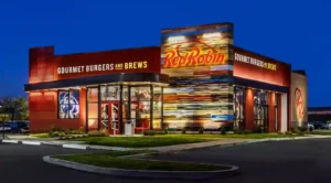 Exterior of a Red Robin restaurant at night, featuring illuminated signage, glass entrance doors, and a well-lit parking lot.