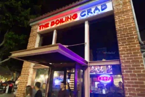 Exterior of The Boiling Crab restaurant at night, featuring a brick facade, neon signage, and large windows with interior lighting.