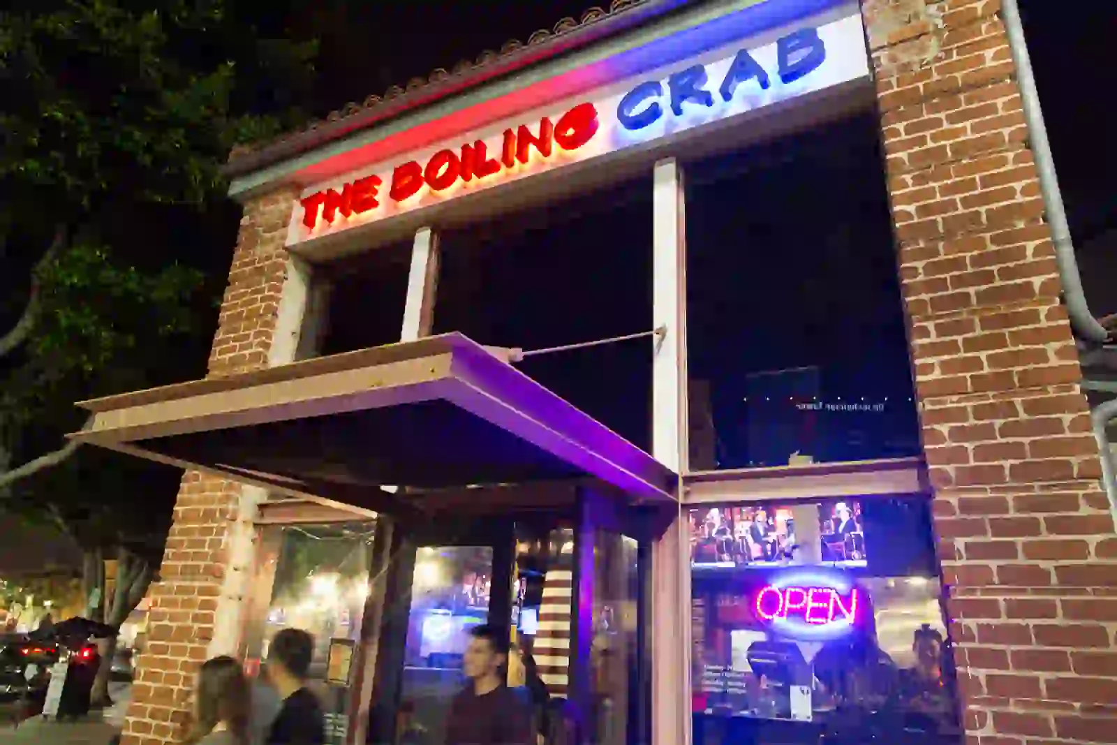 Exterior of The Boiling Crab restaurant at night, featuring a brick facade, neon signage, and large windows with interior lighting.