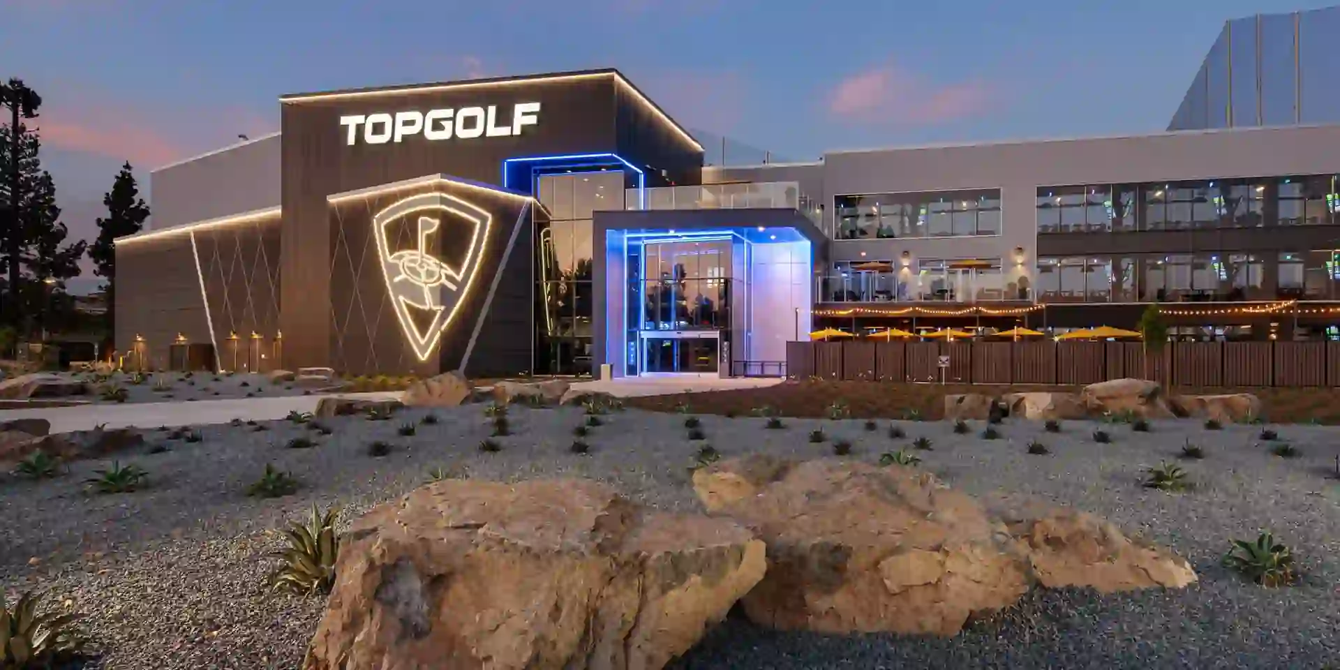 Exterior of a Topgolf facility featuring sleek architecture, illuminated signage, and a modern design with multiple levels.