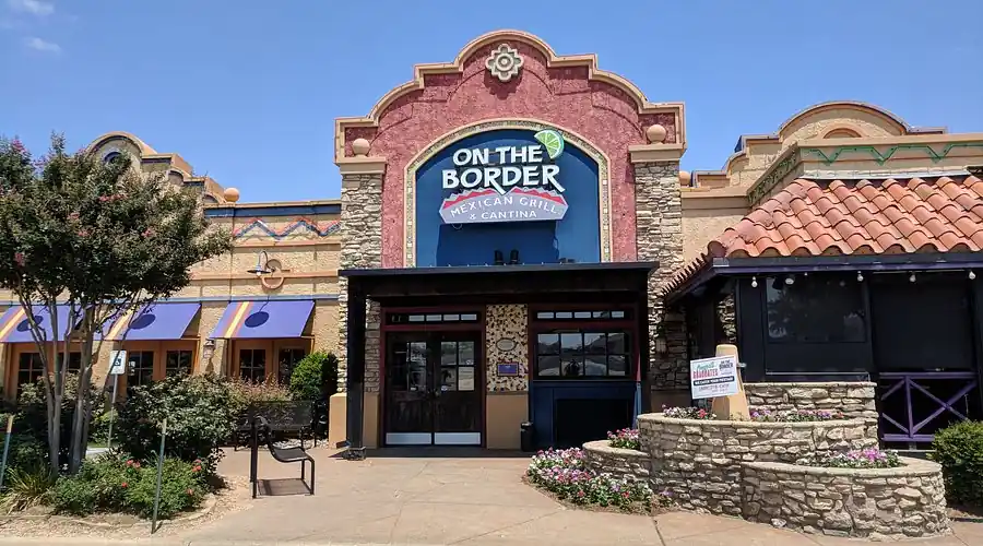 Front entrance of an "On The Border" Mexican Grill & Cantina restaurant with colorful architecture and landscaping.