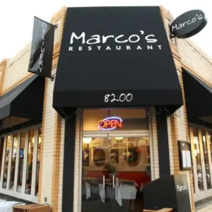 Front entrance of Marco’s Restaurant with black awning, neon open sign, and street number 8200.