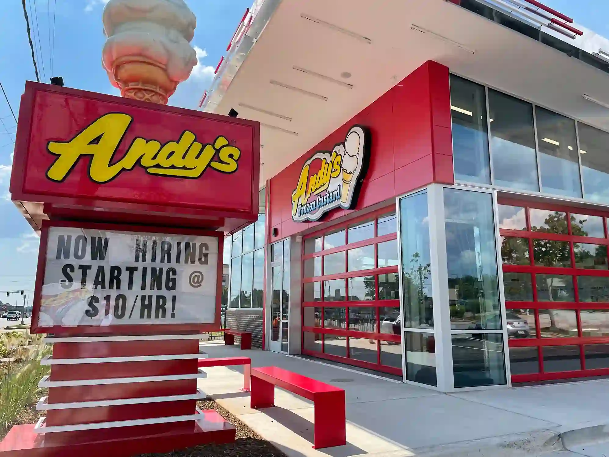 Front exterior of Andy's Frozen Custard with red accents, large glass windows, and a hiring sign advertising $10/hour starting wage.