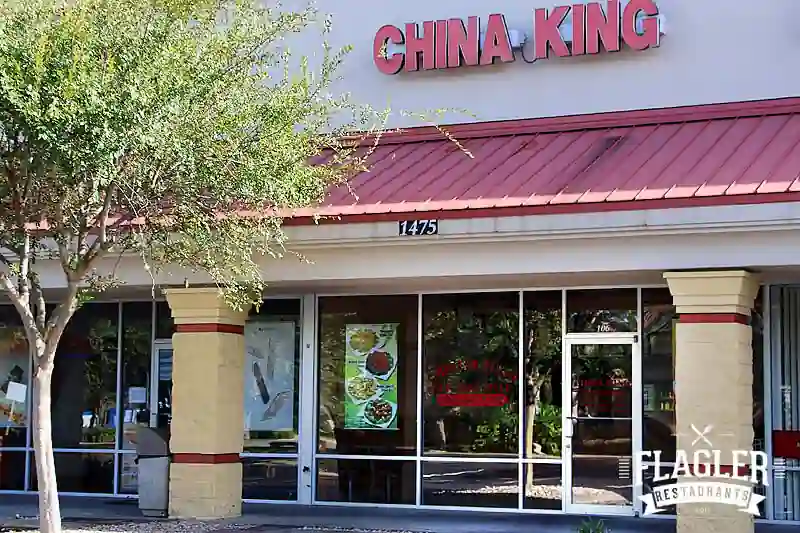 Exterior view of China King restaurant with bold red signage, address number 1475, food posters in the windows, and a tree adding greenery to the front entrance.