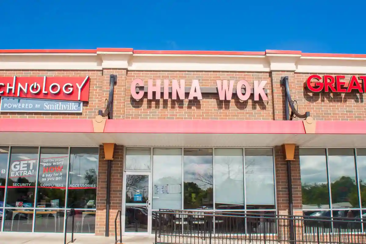 Front view of China Wok restaurant next to Smithville Technology store; features brick facade, red awning, entrance ramp, and window ads for security and phone plans—restaurant entrance clearly marked.