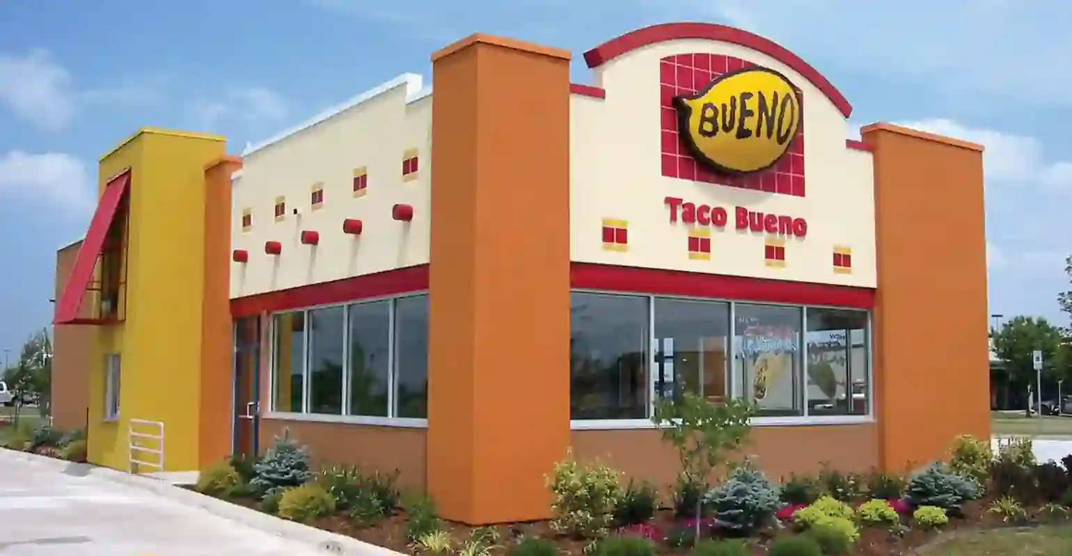 Bright and colorful exterior of a Taco Bueno restaurant with a large "Bueno" sign and neatly maintained landscaping.